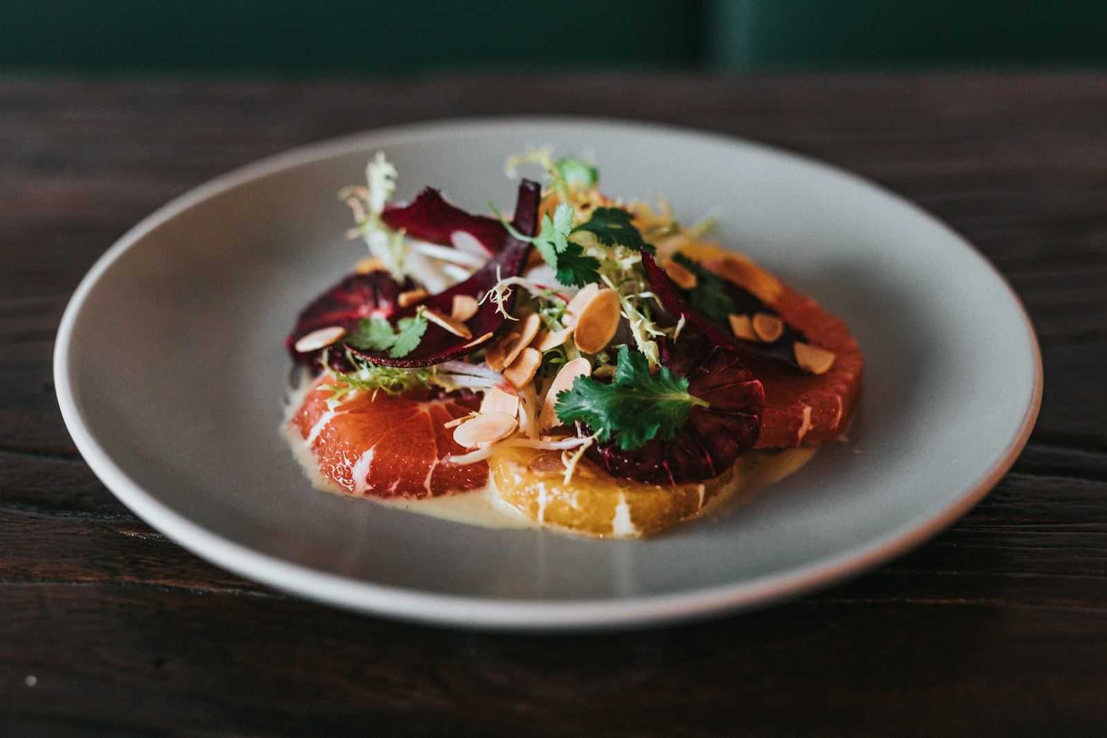 Beet carpaccio with citrus, greens, and toasted almonds on a matte grey plate