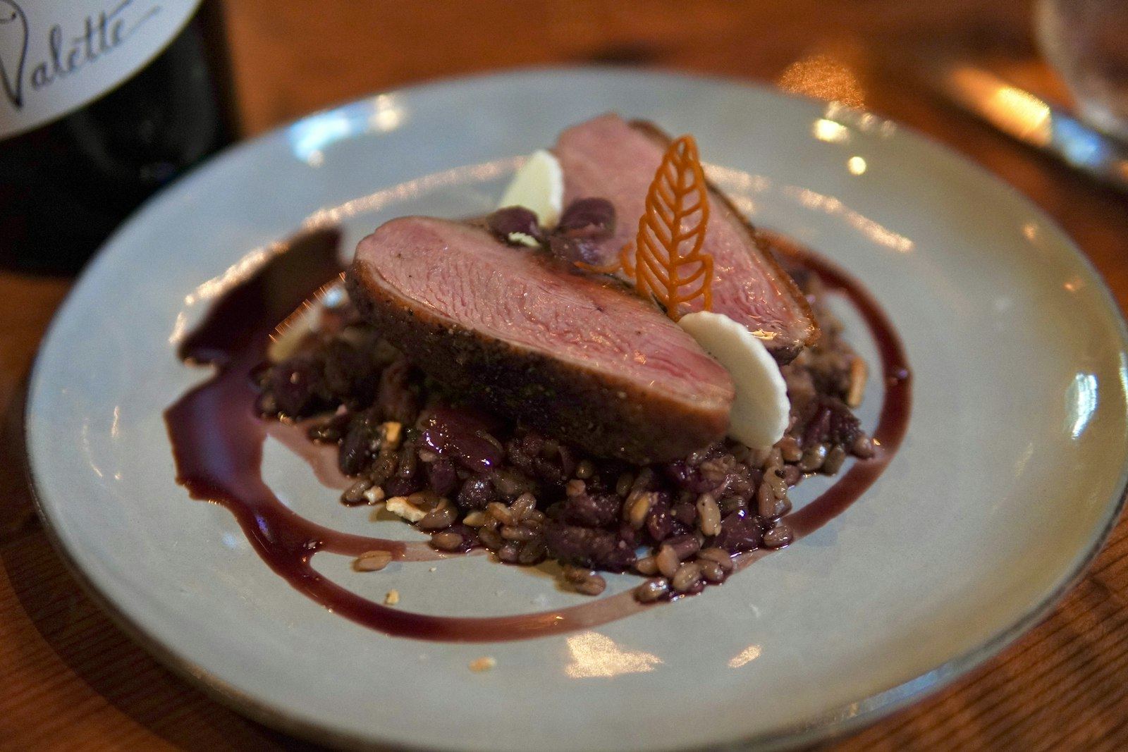 Sliced duck breast with berry reduction, plated at a dimly lit table