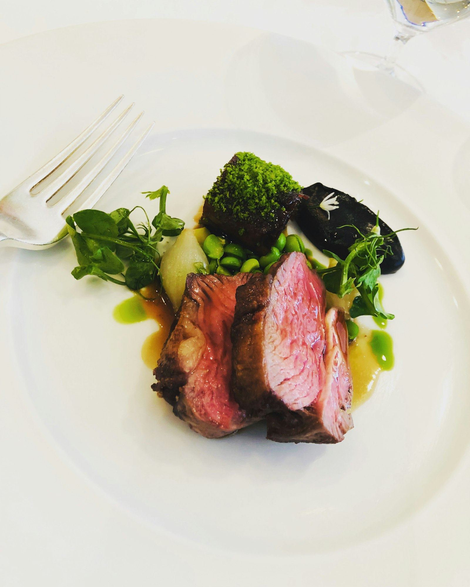 Sliced dry-aged ribeye with pea purée, herbs, and jus on a white plate