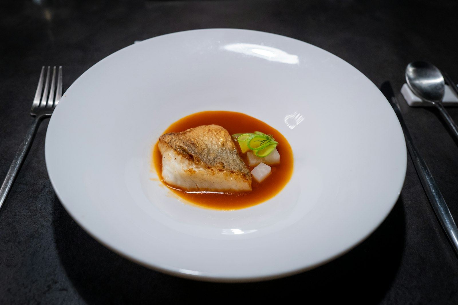 Crispy-skin turbot fillet in amber broth on a white plate