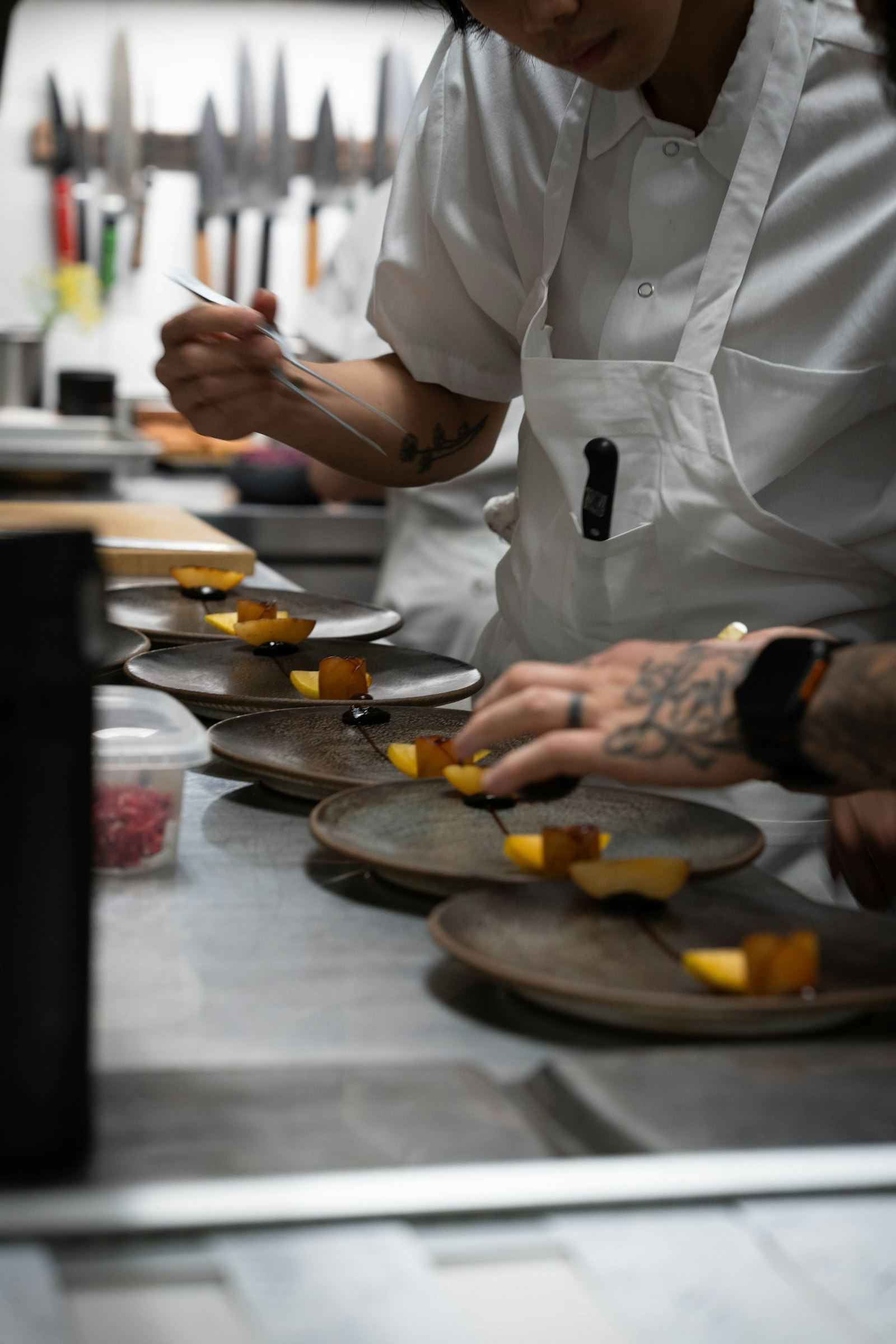 Chef plating a dish with tweezers under kitchen light